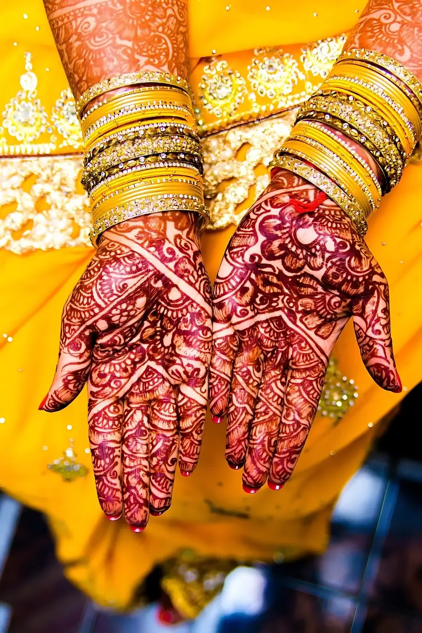 Close-up of intricately designed henna on hands adorned with bangles, highlighting the bridal henna service at Bristol Beauty Line.